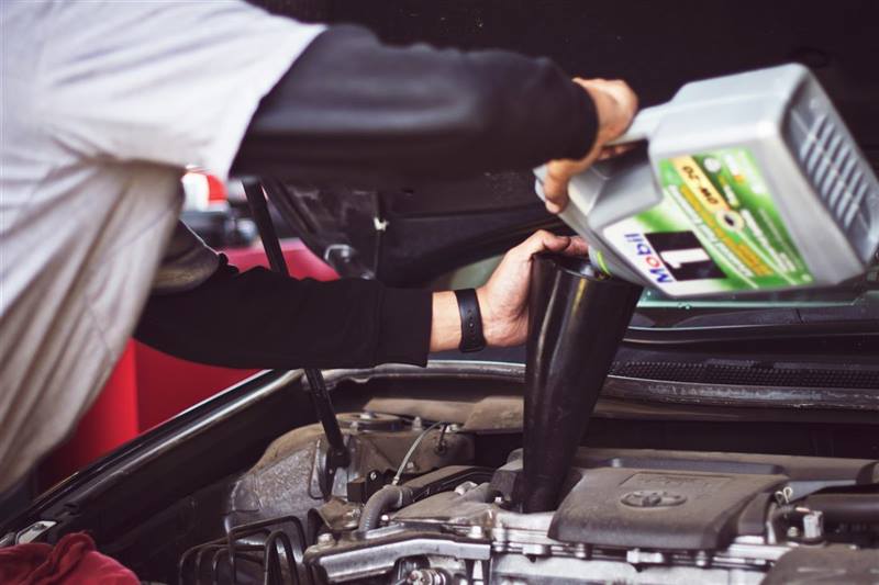 A mechanic pouring fresh motor oil into a car engine during an oil change