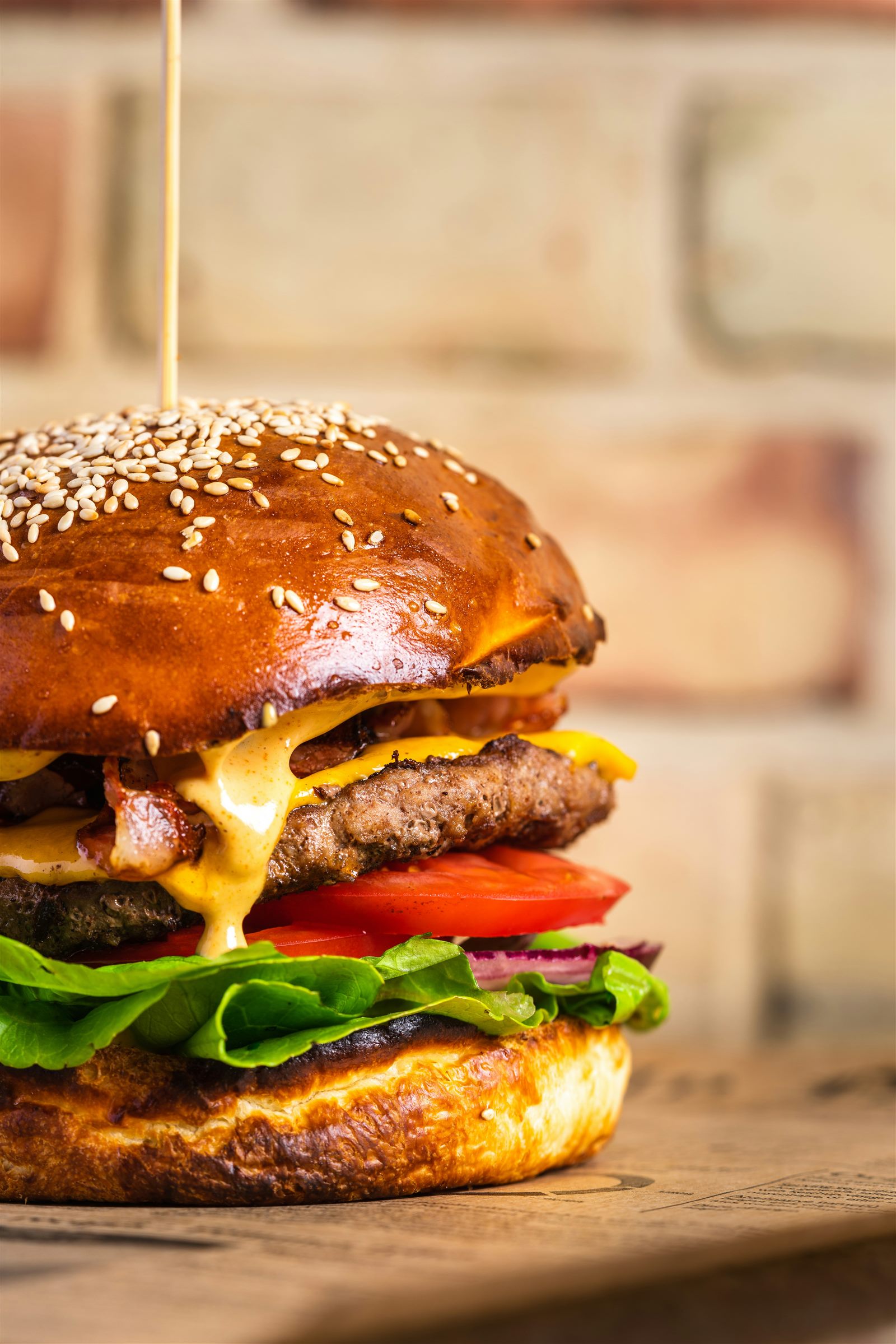 A double cheeseburger on a brioche bun with lettuce and tomato against a brick wall
